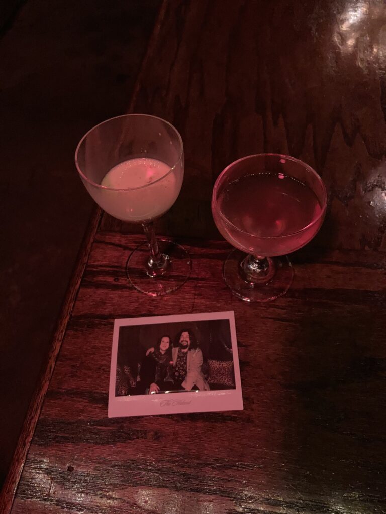 A polaroid picture and two cocktails  sitting on a bar table